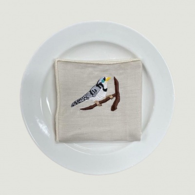 Guardanapo bege bordado com pássaro sobre prato branco