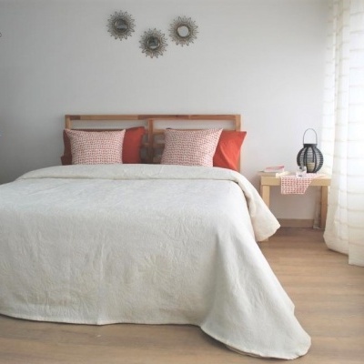Quarto com cama de madeira clara vestida com colcha branca e almofadas vermelhas e bege, decoração minimalista e luz natural.