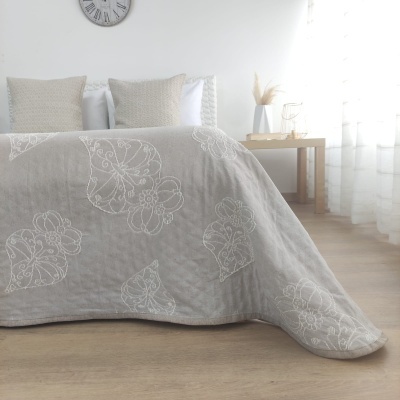 Colcha bege com padrão floral branco bordado em cama em quarto iluminado