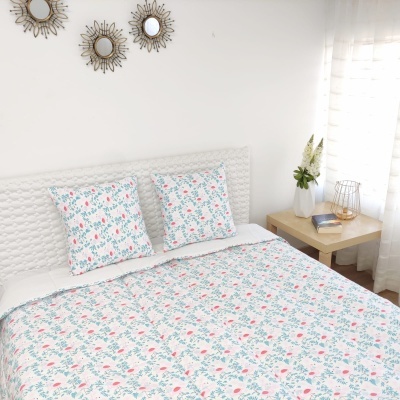 Colcha e almofadas florais em cama branca com mesa de cabeceira e espelhos redondos na parede