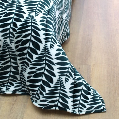 Tecido branco com padrão de folhas pretas cobrindo chão de madeira clara