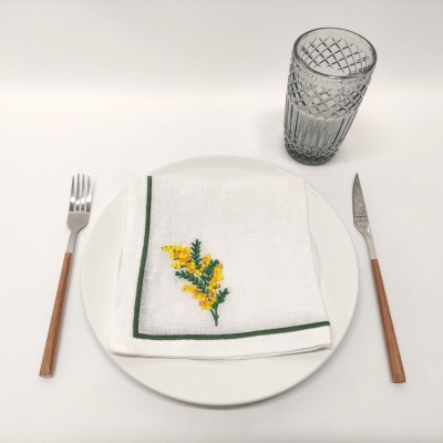 Conjunto de jantar com prato branco, guardanapo bordado, talheres com cabos de madeira e copo de vidro cinza