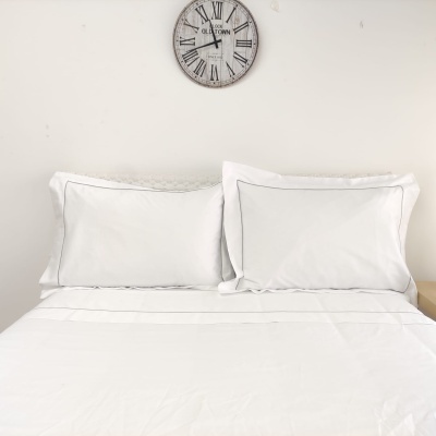 Cama com roupa de cama branca e relógio redondo na parede