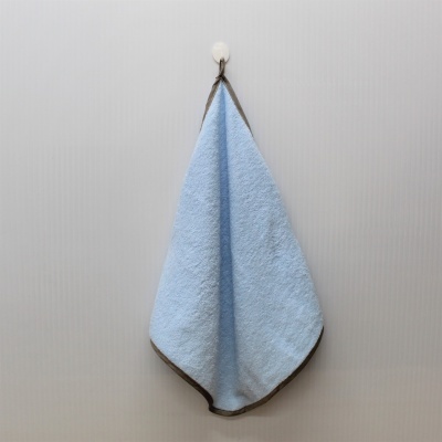 Toalha azul clara com borda castanha pendurada num gancho branco numa parede cinzenta