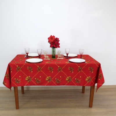 Mesa com toalha vermelha decorada com flores e frutos, pratos, copos, bonecos de rena dourados e vaso com flores vermelhas
