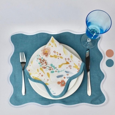 Conjunto de jantar com prato branco, guardanapo floral, placemat azul, talheres metálicos e copo azul