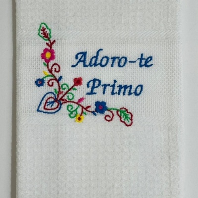 Toalha branca com bordado floral colorido e texto em azul 'Adoro-te Primo'