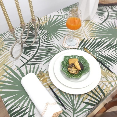 Mesa com toalha de folhas, pratos brancos e verdes com bolachas, castiçal dourado e copo com bebida laranja