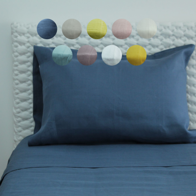 Travesseiro com fronha azul escura sobre cama com lençóis azuis e cabeceira branca acolchoada