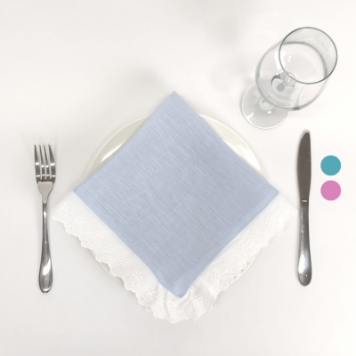Conjunto de mesa com prato branco, guardanapo azul sobre guardanapo branco bordado, talheres de metal e taça de vinho