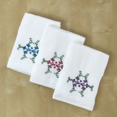 Três toalhas de mão brancas com bordados florais coloridos sobre superfície castanha