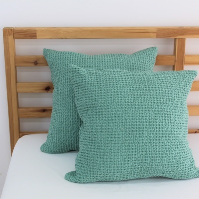 Almofadas verdes de tecido com textura numa cama com cabeceira de madeira clara