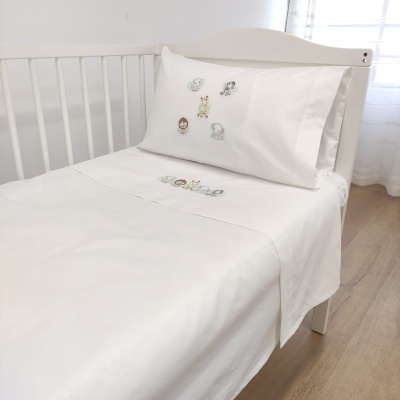Cama de berço branca com lençol e fronha decorada com personagens infantis