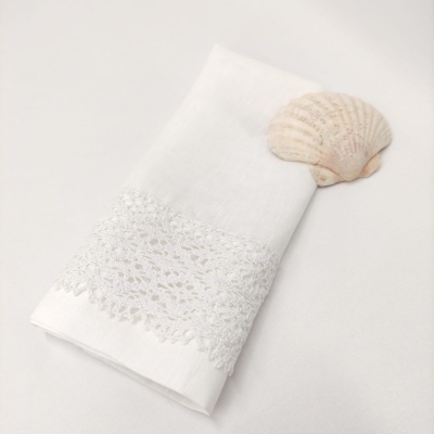 Guardanapo branco com renda ao lado de uma concha marinha clara