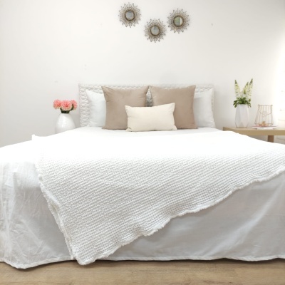 Quarto com cama de lençol branco e cobertor branco, almofadas bege e branco, decoração minimalista com flores e espelhos na parede