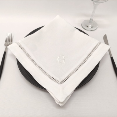 Serviço de mesa com guardanapo branco bordado com monograma, prato preto, talheres e copo