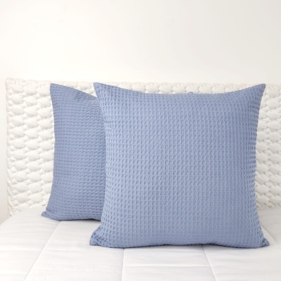 Duas almofadas quadradas azul-claro em tecido com padrão waffle numa cama branca