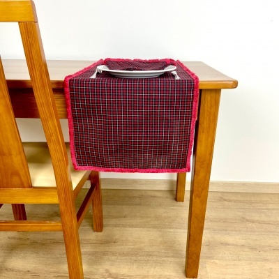 Descanso para prato em tecido quadriculado vermelho, preto e branco com borda vermelha numa mesa de madeira clara.