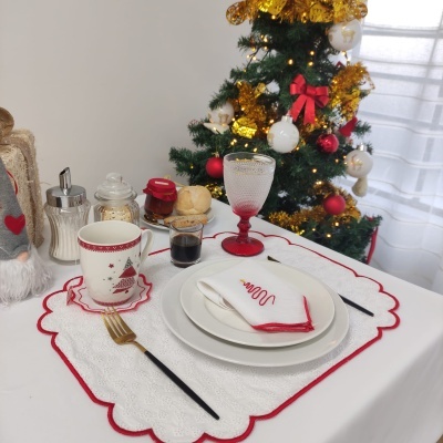 Conjunto de mesa de Natal com pratos, guardanapo, copo, caneca e talheres junto a uma árvore de Natal decorada