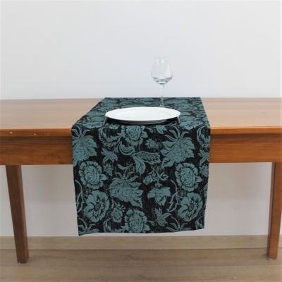 Caminho de mesa com padrão floral azul e preto sobre mesa de madeira clara com prato branco e copo de vinho