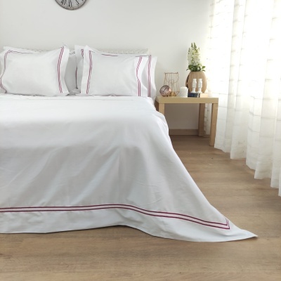 Conjunto de cama branco com riscas vermelhas, lençóis e fronhas, mesa de cabeceira com vaso de flores, piso de madeira clara