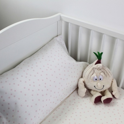 Berço branco com almofada estampada e peluche de alho sorridente.