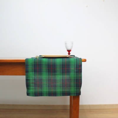 Toalha de mesa verde com padrão de quadros na mesa de madeira com prato e copo.