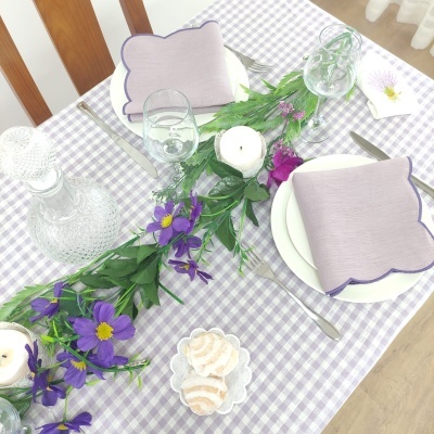 Mesa posta com toalha xadrez lilás e branco, flores roxas, velas, guardanapos lilases e copos de vidro