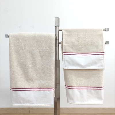 Duas toalhas bege com faixa branca e linhas vermelhas penduradas num suporte metálico prateado
