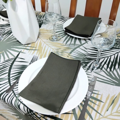 Mesa posta com guardanapos cinza escuro, pratos brancos e toalha de mesa com padrão de folhas tropicais