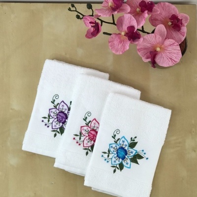 Três toalhas brancas bordadas com flores coloridas ao lado de flores rosas