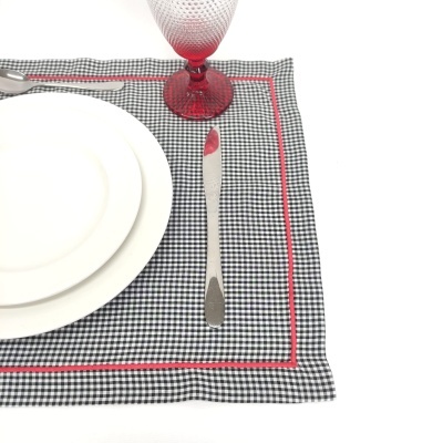 Jogo americano xadrez preto e branco com borda vermelha, pratos brancos, faca de metal e copo vermelho.