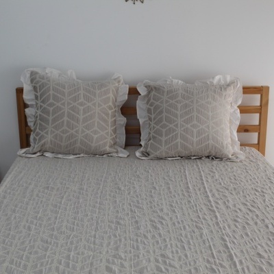 Cama com colcha e almofadas cinzentas com padrão geométrico e cabeceira de madeira clara