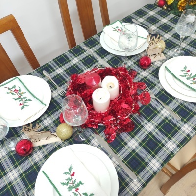 Mesa de jantar decorada com toalha xadrez, guardanapos de Natal, velas e enfeites natalícios