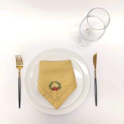 Mesa posta com prato branco, guardanapo amarelo bordado, talheres pretos e dourados e copo transparente