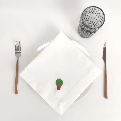 Conjunto de mesa com talheres de madeira, prato branco, guardanapo branco bordado com árvore e copo transparente com padrão.