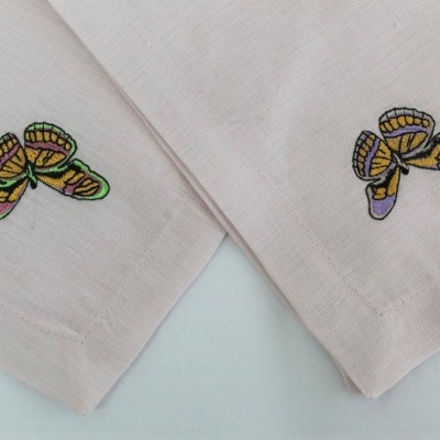 Panos de algodão bege claro com bordado de borboletas coloridas nas extremidades