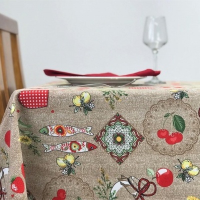Toalha de mesa estampada com peixes, cerejas, abelhas e formas geométricas, em mesa com cadeira de madeira