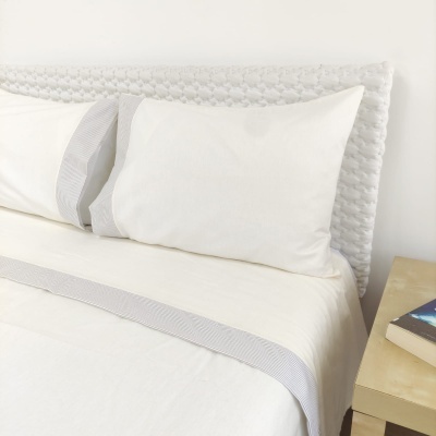 Cama com cabeceira branca trançada e roupa de cama branca com faixa cinza