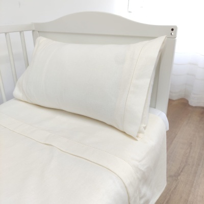 Capa de almofada e lençol brancos em cama branca de madeira, chão de madeira clara e cortinas brancas ao fundo
