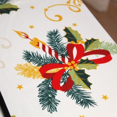 Tecido branco decorado com ramo de pinheiro, folhas de azevinho, laço vermelho e vela listrada acesa