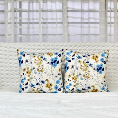 Duas almofadas florais azuis e amarelas sobre cama branca com cabeceira texturizada