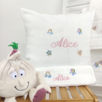 Almofada e toalha brancas bordadas com o nome Alice e pequenos desenhos coloridos, com peluche de alho à esquerda