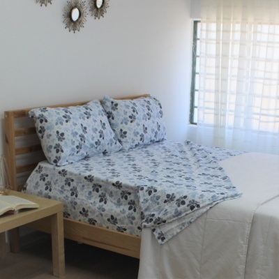 Cama de madeira com roupa de cama floral azul e cinza em quarto iluminado