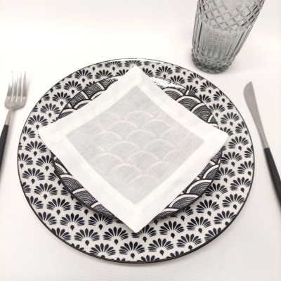 Conjunto de prato grande e pequeno com padrão preto e branco, guardanapo branco, talheres preto e copo de vidro texturizado