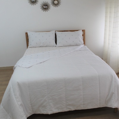 Cama de casal com edredão branco e almofadas brancas com pequenos desenhos finos