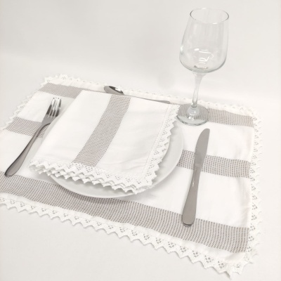 Conjunto de loiça com guardanapo e jogo americano de tecido branco com bordado cinzento e renda, talheres e taça de vidro