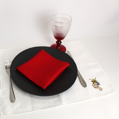 Conjunto de jantar com prato preto, guardanapo vermelho, talheres de metal, copo de vidro com base vermelha e toalhete branco bordado