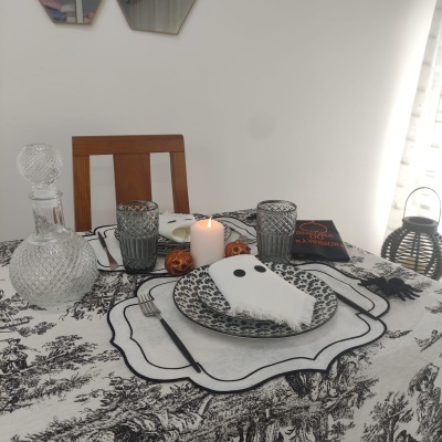 Mesa posta com toalha preta e branca, pratos e guardanapo, vela acesa e garrafa de vidro