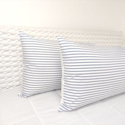 Dois almofadas com riscas azuis e brancas em cima de uma cama branca com cabeceira texturada clara
